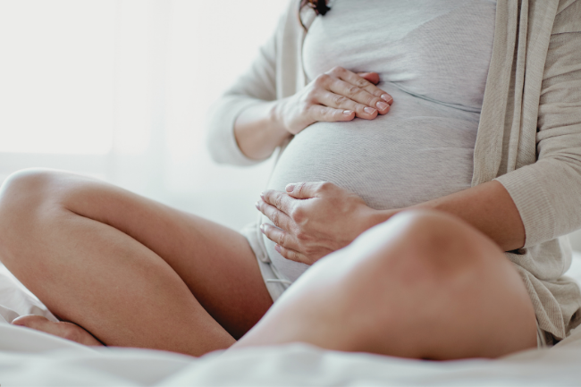 Bauch einer schwangeren Frau, umfasst von beiden Händen der Schwangeren, während sie den Hypnobirhting und Selbstliebe Audiokurs hört